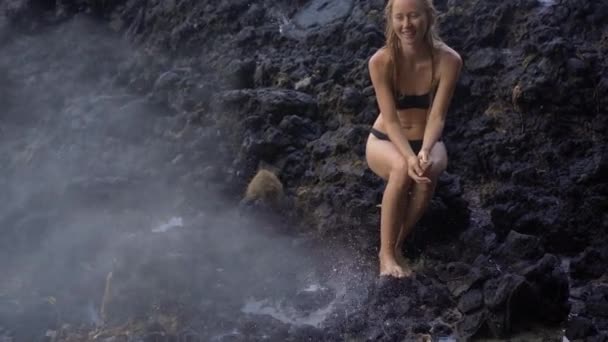 Superslowmotion tiro de uma jovem mulher apreciando as fontes ou gêiseres feitos por natureza em rochas vulcânicas perto da praia de areia branca na ilha de Bali — Vídeo de Stock