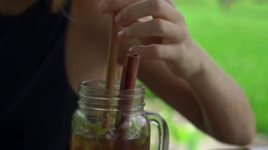 Arka planda pirinç tarlası olan bir sokak kafesinde nane ve limonla buzlu çay içen genç bir kadının yakın çekim fotoğrafı