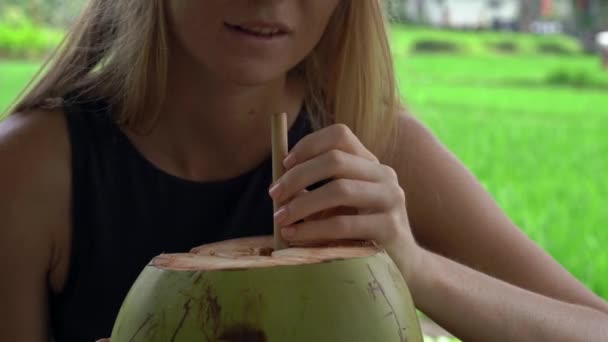 Primer plano de una joven bebiendo cocnut joven en un café de la calle con un campo de arroz en un fondo — Vídeos de Stock