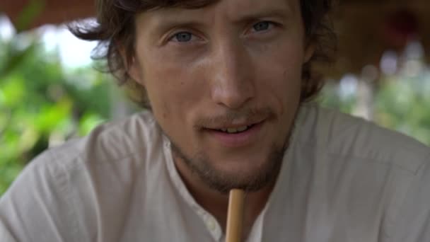 Close-up shot van een jonge man die ijsthee drinkt met mint en citroen in een straat café met een rijstveld op een achtergrond — Stockvideo
