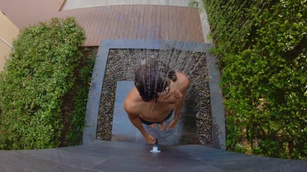 Slowmotion shot of a young man that takes a shower in a tropical garden. Holidays in a tropical resort concept. Young man vlogger makes a video of himself taking a shower in a tropical hotel — Stockvideo