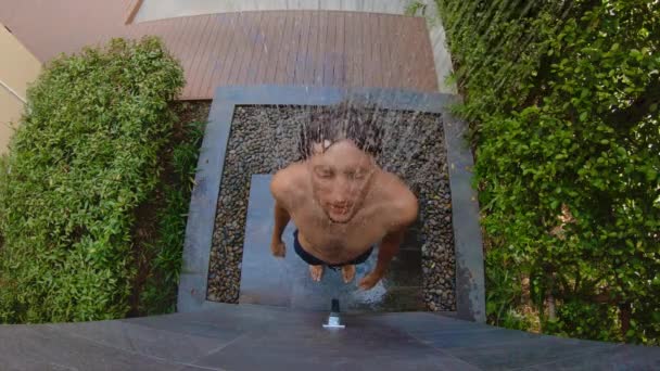 Prise de vue au ralenti d'un jeune homme qui prend une douche dans un jardin tropical. Vacances dans un concept de station tropicale. Jeune homme vlogger fait une vidéo de lui-même prendre une douche dans un hôtel tropical — Video