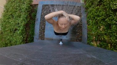 Genç bir kadının yavaş çekim çekim tropikal bir bahçede bir duş alır. Tropik bir tatil konseptinde tatiller. Genç kadın vlogger kendini tropikal bir otelde duş alarak bir video yapar