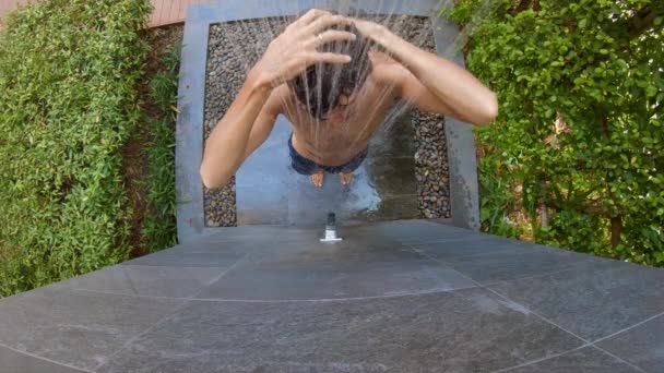 Повільний знімок молодого чоловіка, який приймає душ у тропічному саду. Відпочинок в концепції тропічного курорту. Молодий чоловік робить відео про себе, приймаючи душ в тропічному готелі — стокове відео