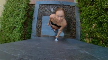 Genç bir kadının yavaş çekim çekim tropikal bir bahçede bir duş alır. Tropik bir tatil konseptinde tatiller. Genç kadın vlogger kendini tropikal bir otelde duş alarak bir video yapar