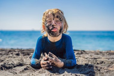 Kara Cuma konsepti. Okyanusta yüzmeden önce kirli Siyah yüzü oturan ve siyah kum denizi sahilinde oynayan gülümseyen çocuk. Aile aktif yaşam tarzı ve çocuklarla yaz tatilinde su eğlence