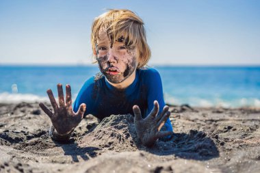 Kara Cuma konsepti. Okyanusta yüzmeden önce kirli Siyah yüzü oturan ve siyah kum denizi sahilinde oynayan gülümseyen çocuk. Aile aktif yaşam tarzı ve çocuklarla yaz tatilinde su eğlence