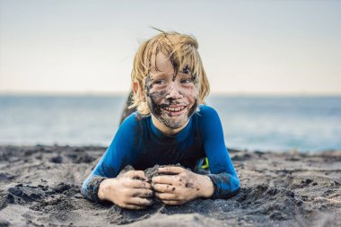 Kara Cuma konsepti. Okyanusta yüzmeden önce kirli Siyah yüzü oturan ve siyah kum denizi sahilinde oynayan gülümseyen çocuk. Aile aktif yaşam tarzı ve çocuklarla yaz tatilinde su eğlence
