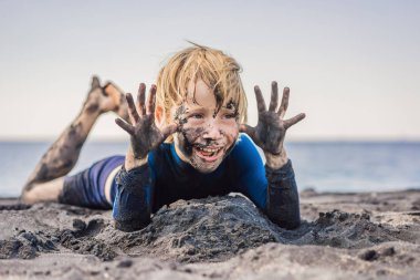 Kara Cuma konsepti. Okyanusta yüzmeden önce kirli Siyah yüzü oturan ve siyah kum denizi sahilinde oynayan gülümseyen çocuk. Aile aktif yaşam tarzı ve çocuklarla yaz tatilinde su eğlence