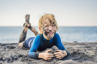 Kara Cuma konsepti. Okyanusta yüzmeden önce kirli Siyah yüzü oturan ve siyah kum denizi sahilinde oynayan gülümseyen çocuk. Aile aktif yaşam tarzı ve çocuklarla yaz tatilinde su eğlence