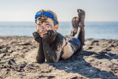 Kara Cuma konsepti. Okyanusta yüzmeden önce kirli Siyah yüzü oturan ve siyah kum denizi sahilinde oynayan gülümseyen çocuk. Aile aktif yaşam tarzı ve çocuklarla yaz tatilinde su eğlence