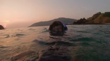 Gün batımında suda selfie videosu çeken genç bir dalgıç, yavaş çekim. Sualtı vlogging