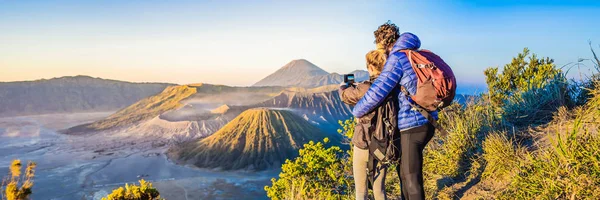 BANNER, FORMATO LARGO Pareja joven hombre y mujer se encuentran con el amanecer en el Parque Nacional Bromo Tengger Semeru en la isla de Java, Indonesia. Disfrutan de magníficas vistas sobre el Bromo o Gunung Bromo en — Foto de Stock