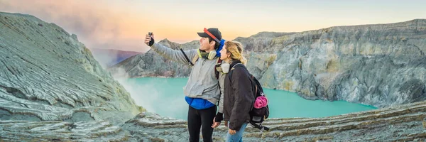 БАННЕР, ЛОНГ ФОРМАТ Юные туристы - мужчина и женщина - стоят на краю кратера вулкана Иволкано или Кава-Иль на индонезийском языке. Известный вулкан, содержащий самую большую в мире кислоту — стоковое фото