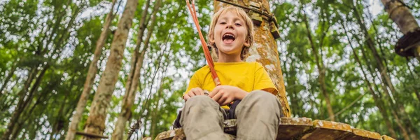 Um rapazinho num parque de cordas. Recreação física ativa da criança ao ar livre no parque. Treinamento para crianças BANNER, LONG FORMAT — Fotografia de Stock