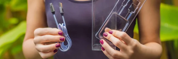 Female hands printed a new wire to charge the phone. The wire was packed in a large number of plastic packaging, which will be thrown into the trash. Zero waste concept. Plastic trash concept BANNER — Stock Photo, Image