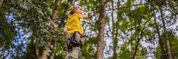 Um rapazinho num parque de cordas. Recreação física ativa da criança ao ar livre no parque. Treinamento para crianças BANNER, LONG FORMAT — Fotografia de Stock