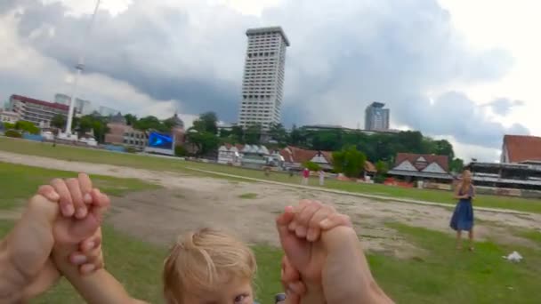 Punto de vista en cámara lenta tipo de toma de un padre girando a su hijo en una plaza Merdeka en Kuala Lumpur. Viajar a Malasia concepto — Vídeos de Stock