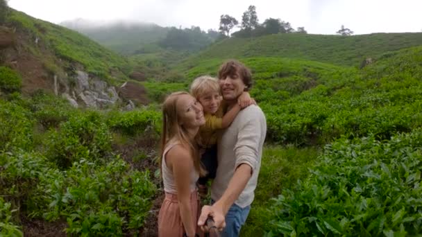 Disparo en cámara lenta. Pareja joven y su hijo hacen una selfie de pie en una gran plantación de té en las montañas — Vídeo de stock