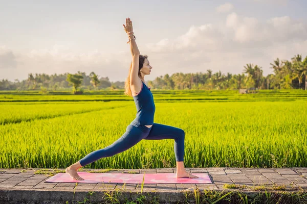 Junge Frau praktiziert Yoga im Freien in Reisfeldern am Morgen während eines Wellness-Retreats in Bali — Stockfoto