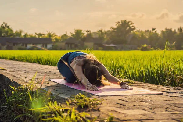 Молодая женщина практикует йогу на открытом воздухе на рисовых полях утром во время оздоровительного отдыха на Бали — стоковое фото
