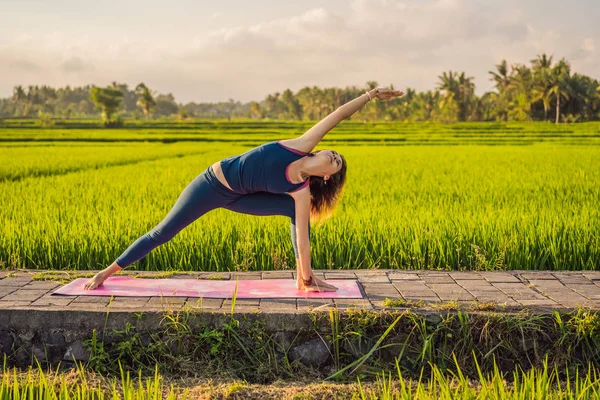 Fiatal nő gyakorlat jóga szabadtéri a rizs mezők a reggel folyamán wellness retreat Bali — Stock Fotó