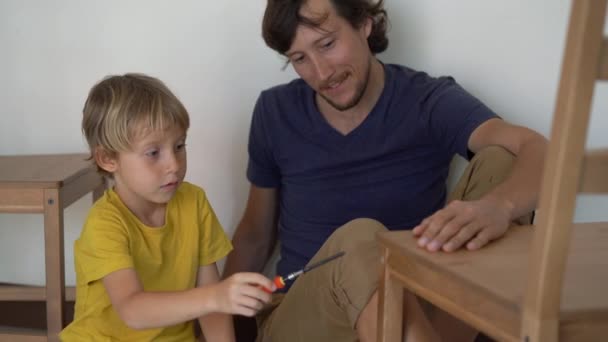 Father and his little son are assembling furniture. They assemble a kitchen chair — Stock Video