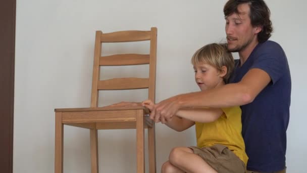 Vader en zijn zoontje zijn het monteren van meubels. Ze monteren een keukenstoel — Stockvideo
