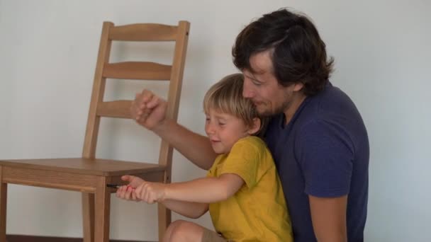 O pai e o filho estão a montar mobília. Eles montam uma cadeira de cozinha — Vídeo de Stock