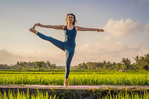 Mujer joven practica yoga al aire libre en campos de arroz por la mañana durante el retiro de bienestar en Bali —  Fotos de Stock