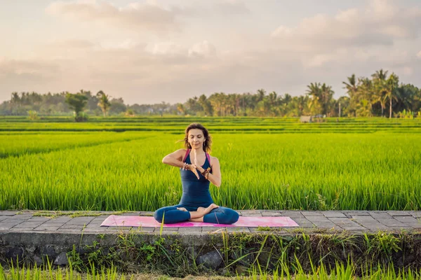 Mujer joven practica yoga al aire libre en campos de arroz por la mañana durante el retiro de bienestar en Bali —  Fotos de Stock