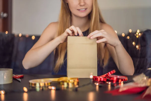 Young woman is packing presents. Present wrapped in craft paper with a red and gold ribbon for christmas, birthday, mothers day or valentine