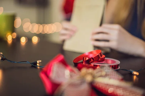 La joven está empacando regalos. Regalo envuelto en papel artesanal con cinta roja y dorada para Navidad, cumpleaños, día de la madre o San Valentín —  Fotos de Stock