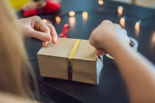 年轻女子正在打包礼物。礼物包裹在工艺纸与红色和金色的丝带圣诞节，生日，母亲节或情人节 — 图库照片