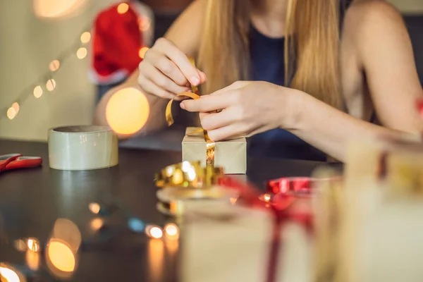 Η νεαρή γυναίκα μαζεύει δώρα. Παρόν τυλιγμένο σε χαρτί χειροτεχνίας με μια κόκκινη και χρυσή κορδέλα για τα Χριστούγεννα ή το νέο έτος. Η γυναίκα κάνει μια έλευση ημερολόγιο για το παιδί της — Φωτογραφία Αρχείου