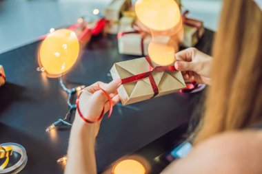 Genç kadın hediyeleri paketlikiyor. Noel, doğum günü, anneler günü veya sevgililer günü için kırmızı ve altın kurdele ile zanaat kağıt sarılmış hediye