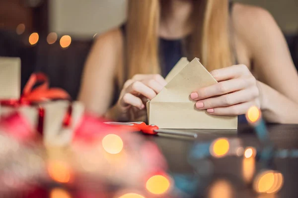 Η νεαρή γυναίκα μαζεύει δώρα. Παρόν τυλιγμένο σε χαρτί χειροτεχνίας με μια κόκκινη και χρυσή κορδέλα για τα Χριστούγεννα, γενέθλια, ημέρα της μητέρας ή του Αγίου Βαλεντίνου — Φωτογραφία Αρχείου