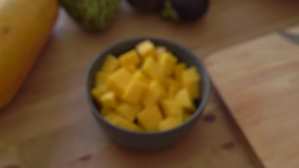 Mango blokjes in een grijze keramische kom en veel tropisch fruit lag op een tafel — Stockvideo