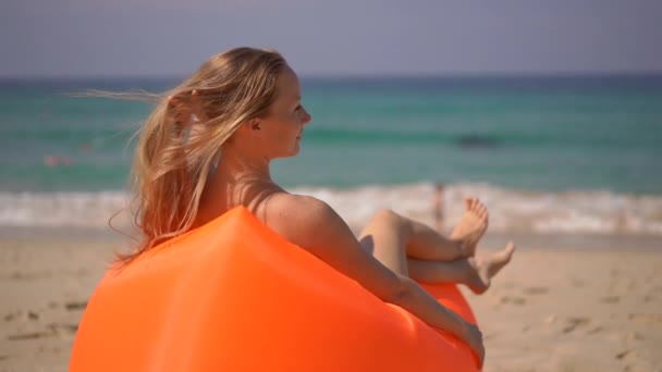 Superslowmotion shot van een jonge vrouw ontspannen op een opgeblazen sofa op een tropisch strand — Stockvideo