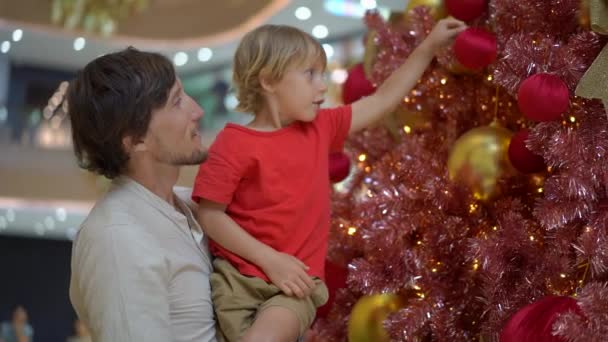 Slowmotion shot van een kleine jongen hangt rode kerst decoratie op de rode en gouden kerstboom — Stockvideo