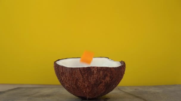 Superslowmotion shot van spatten van kokosmelk na blokjes van tropisch fruit in het op een gele achtergrond gedropt — Stockvideo