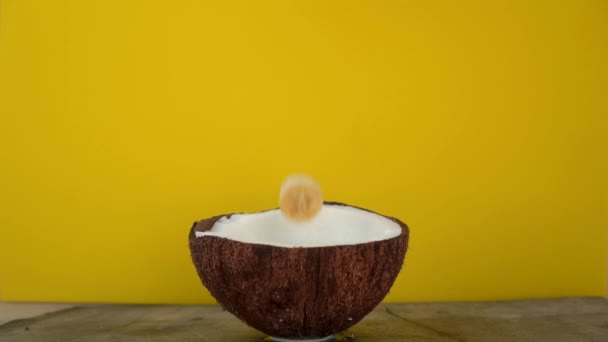 Superslowmotion tiro de salpicos de leite de coco após cubos de frutas tropicais sendo jogado nele em um fundo amarelo — Vídeo de Stock