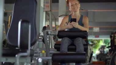 Spor salonunda genç bir kadın elinde gözlerinin önünde bir telefon tutarak egzersiz yapıyor. Tüm dikkatler telefonda. Sosyal ağlara bağımlılık kavramı. Mobil bağımlılık kavramı