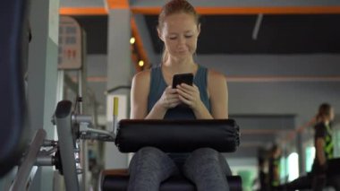 Spor salonunda genç bir kadın elinde gözlerinin önünde bir telefon tutarak egzersiz yapıyor. Tüm dikkatler telefonda. Sosyal ağlara bağımlılık kavramı. Mobil bağımlılık kavramı