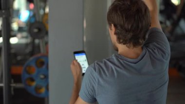 Spor salonunda genç bir adam elinde gözlerinin önünde bir telefon tutarak egzersiz yapıyor. Tüm dikkatler telefonda. Sosyal ağlara bağımlılık kavramı. Mobil bağımlılık kavramı