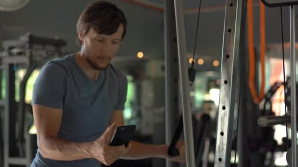 Een jonge man in de sportschool doen oefeningen houden een telefoon voor zijn ogen in zijn handen. Alle aandacht is in de telefoon. Het begrip afhankelijkheid van sociale netwerken. Mobiel verslavings concept — Stockvideo