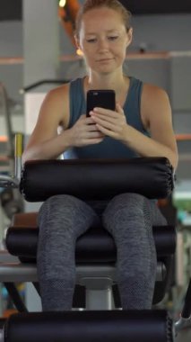 Dikey video. Spor salonunda bir egzersiz bisikleti üzerinde genç bir adam elinde gözlerinin önünde telefon tutarak. Tüm dikkatler telefonda. Sosyal ağlara bağımlılık kavramı. Mobil