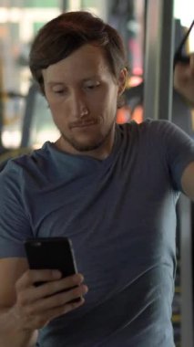Dikey video. Spor salonunda bir egzersiz bisikleti üzerinde genç bir adam elinde gözlerinin önünde telefon tutarak. Tüm dikkatler telefonda. Sosyal ağlara bağımlılık kavramı. Mobil