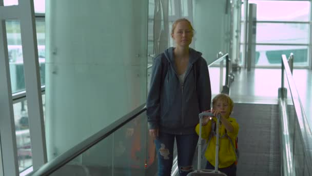 Steadicam disparo de una mujer joven y su hijo pequeño utilizando una escalera mecánica horizontal Travolator en un aeropuerto — Vídeos de Stock