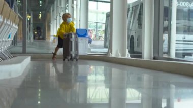 Little boy in a medical face mask playing with a suitcase in an airport
